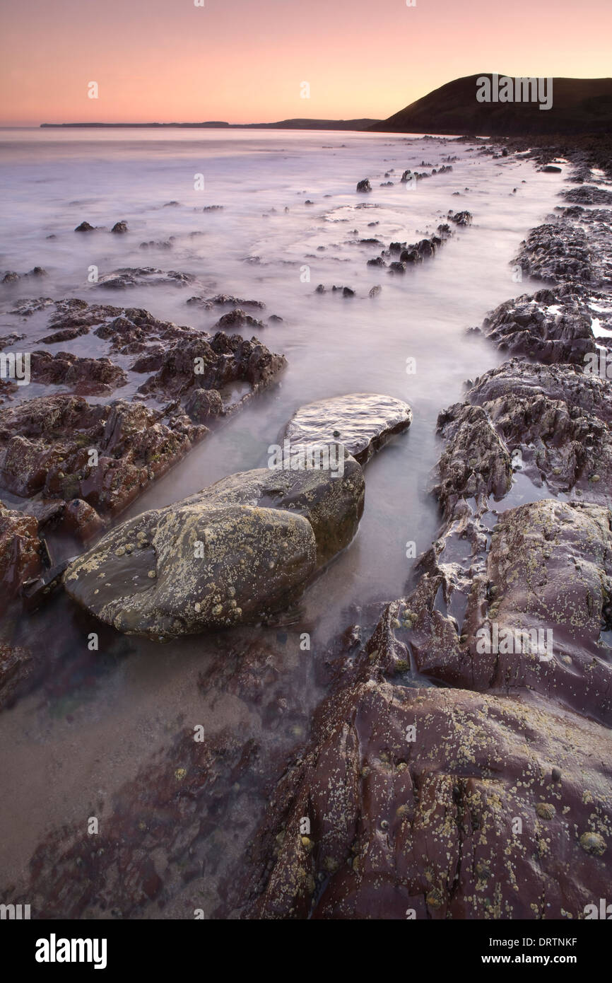 Rocce frastagliate essendo coperto dalla marea al tramonto di Manorbier Beach, Pembrokeshire, South Wales, Regno Unito Foto Stock