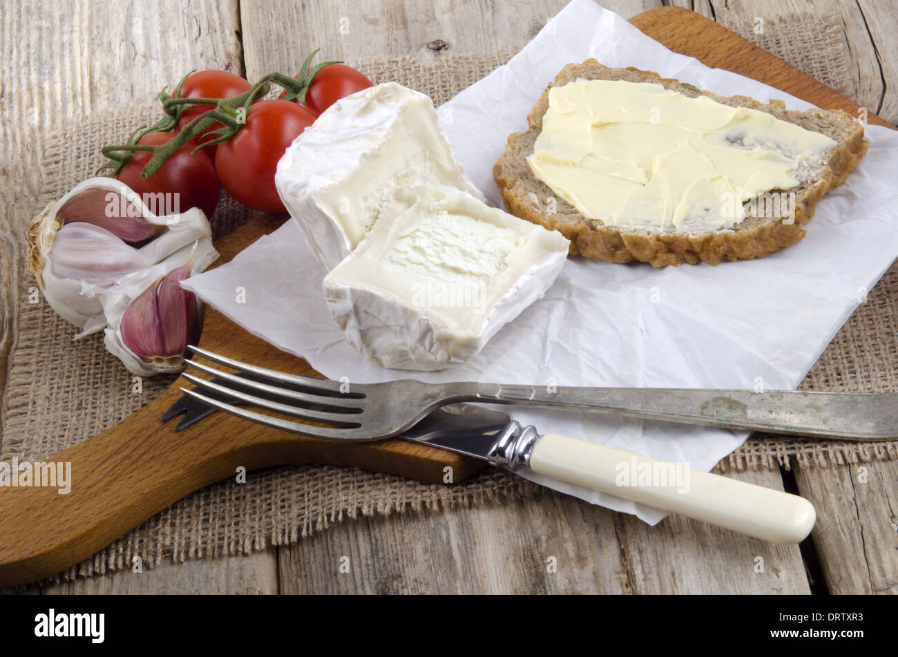 Tavola di legno con formaggio di capra, pane, forchetta e coltello Foto Stock