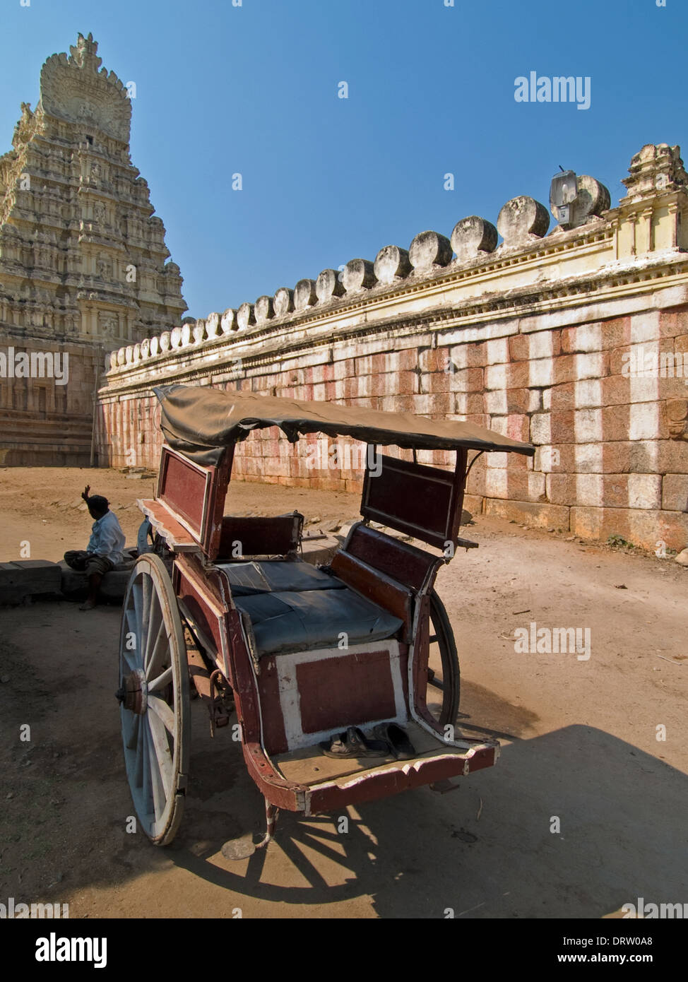 Un piccolo carrello del cavallo è parcheggiato al di fuori del rosso-e-bianco striato pareti di un tempio indù, il suo tower gateway nella distanza. Foto Stock