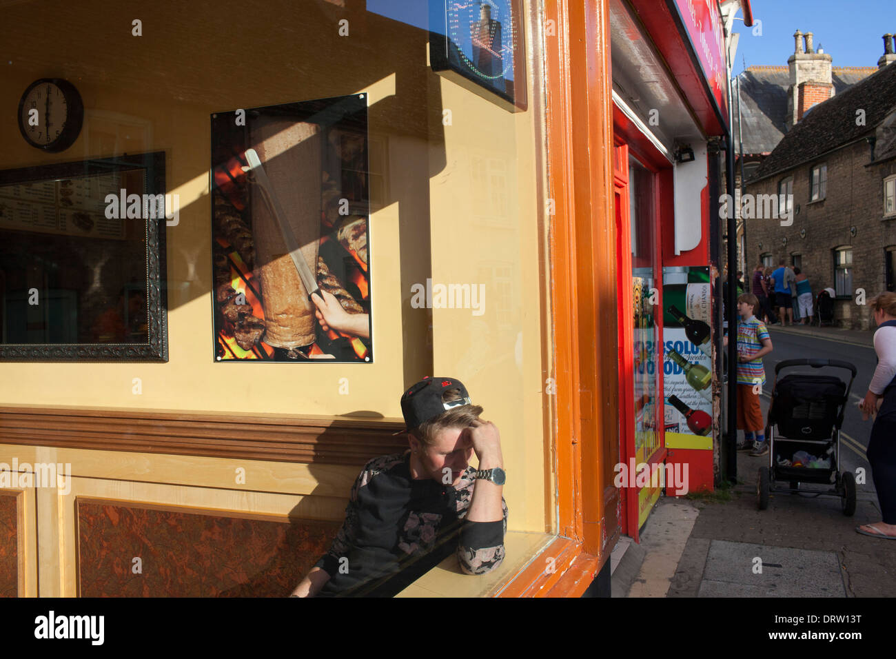 Una gioventù attende il suo ordine in una pizza e kebab house. Foto Stock