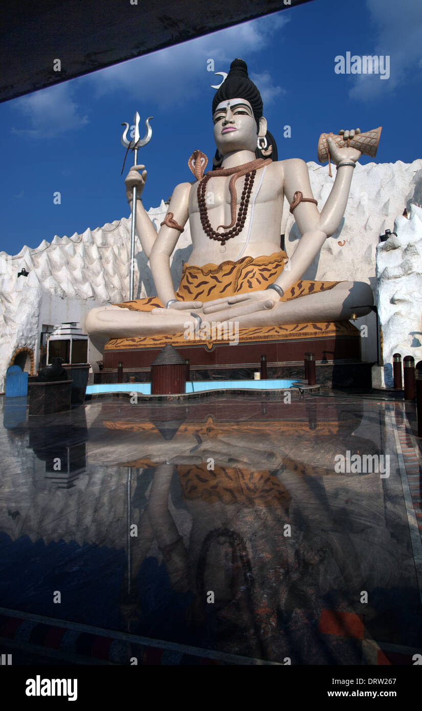 Una moderna statua di un Signore seduto Shiva torreggia su una piscina riflettente in un tempio indiano Foto Stock