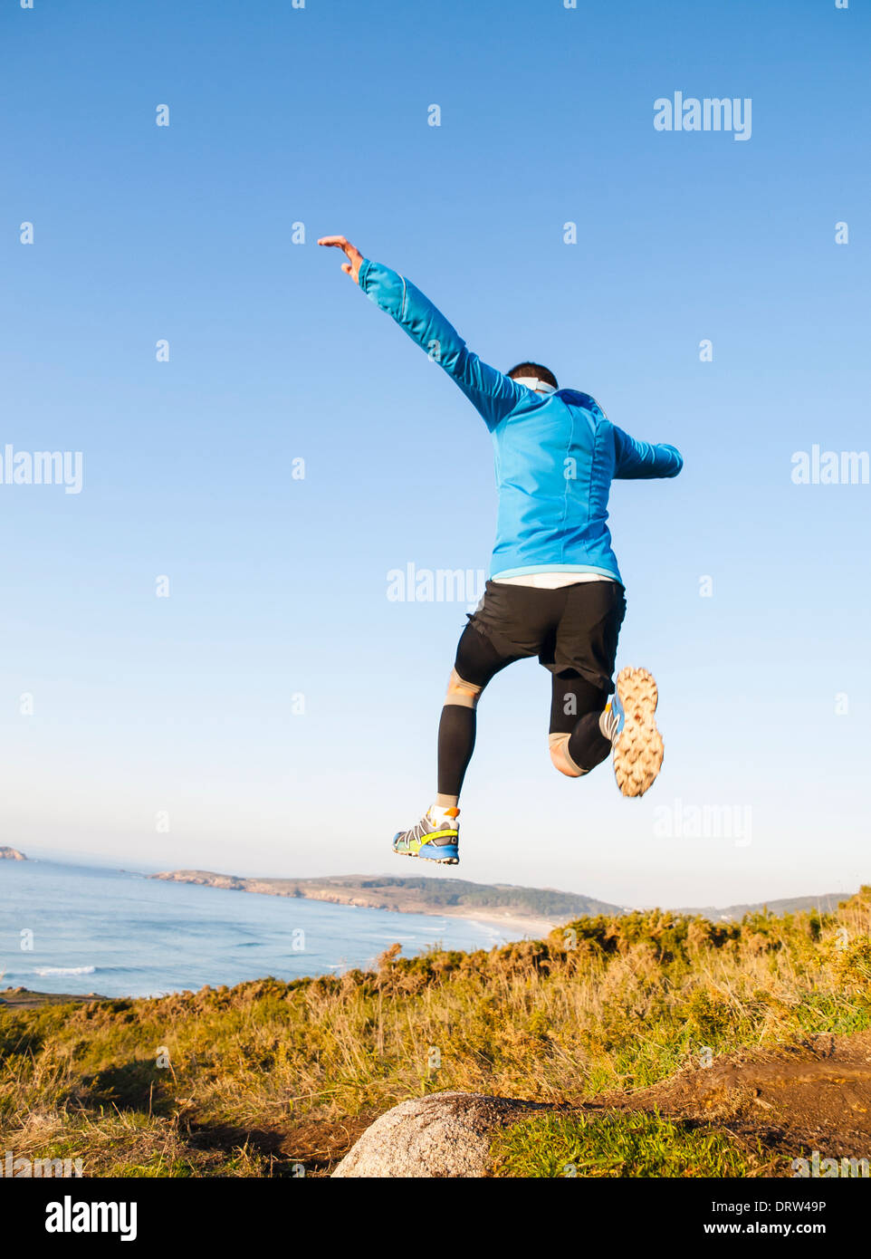 Uomo di dare un grande salto mentre si pratica la corsa su sentiero con un paesaggio costiero in background. Foto Stock