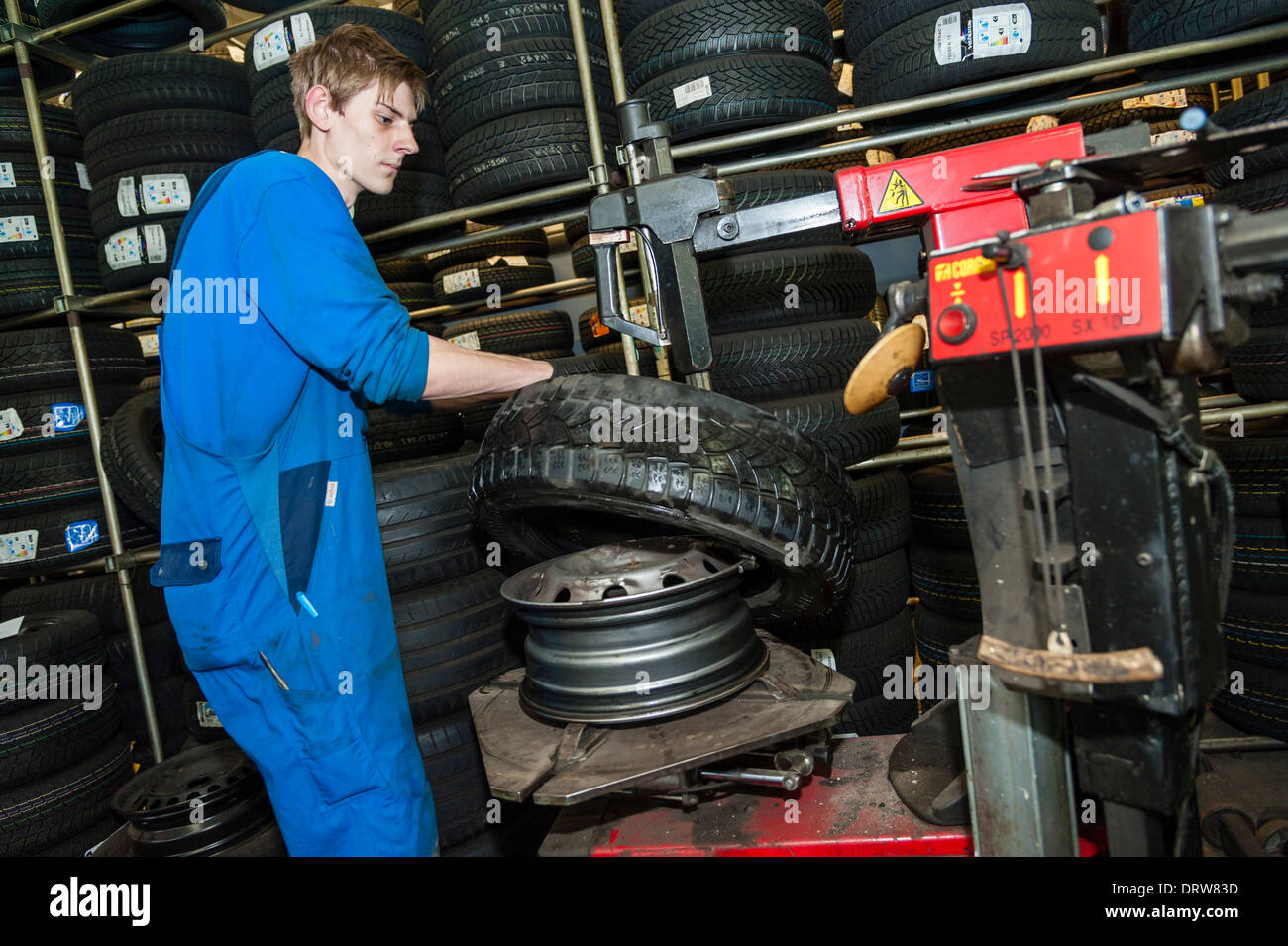 Un meccanico di automobili si inserisce un nuovo pneumatico su di un cerchione di ruota. Foto Stock