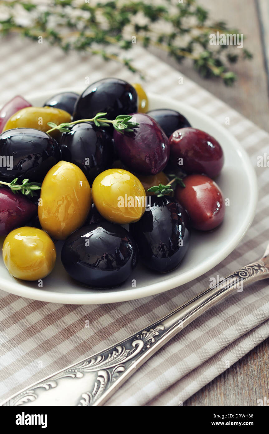Diversi tipi di olive su piastra con forcella sullo sfondo di legno Foto Stock