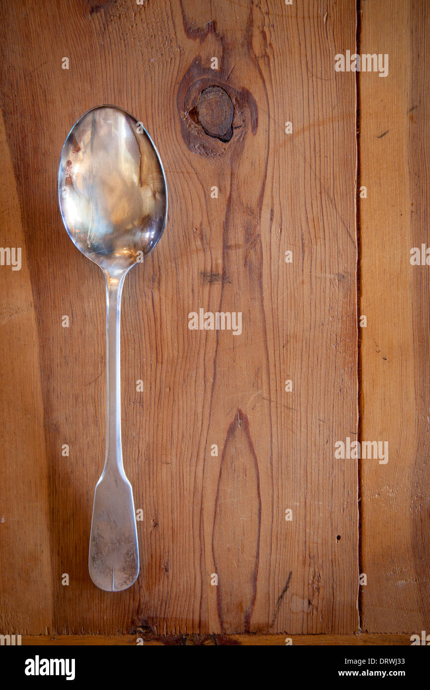 Argento vecchio cucchiaio su asse di legno tabella Foto Stock