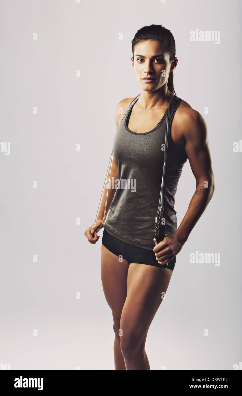 Ritratto di donna attraente atleta holding salto con la corda guardando la telecamera contro uno sfondo grigio. Femmina con corpo muscoloso Foto Stock