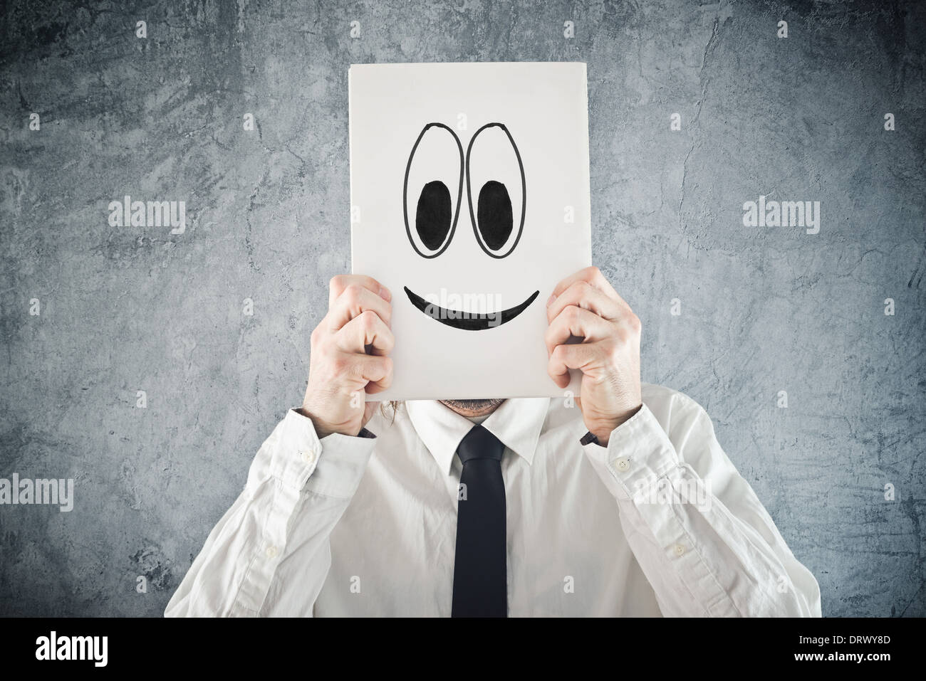 Imprenditore tenendo la carta con faccina sorridente davanti alla sua testa. Happy businessman, ufficio situazione. Foto Stock