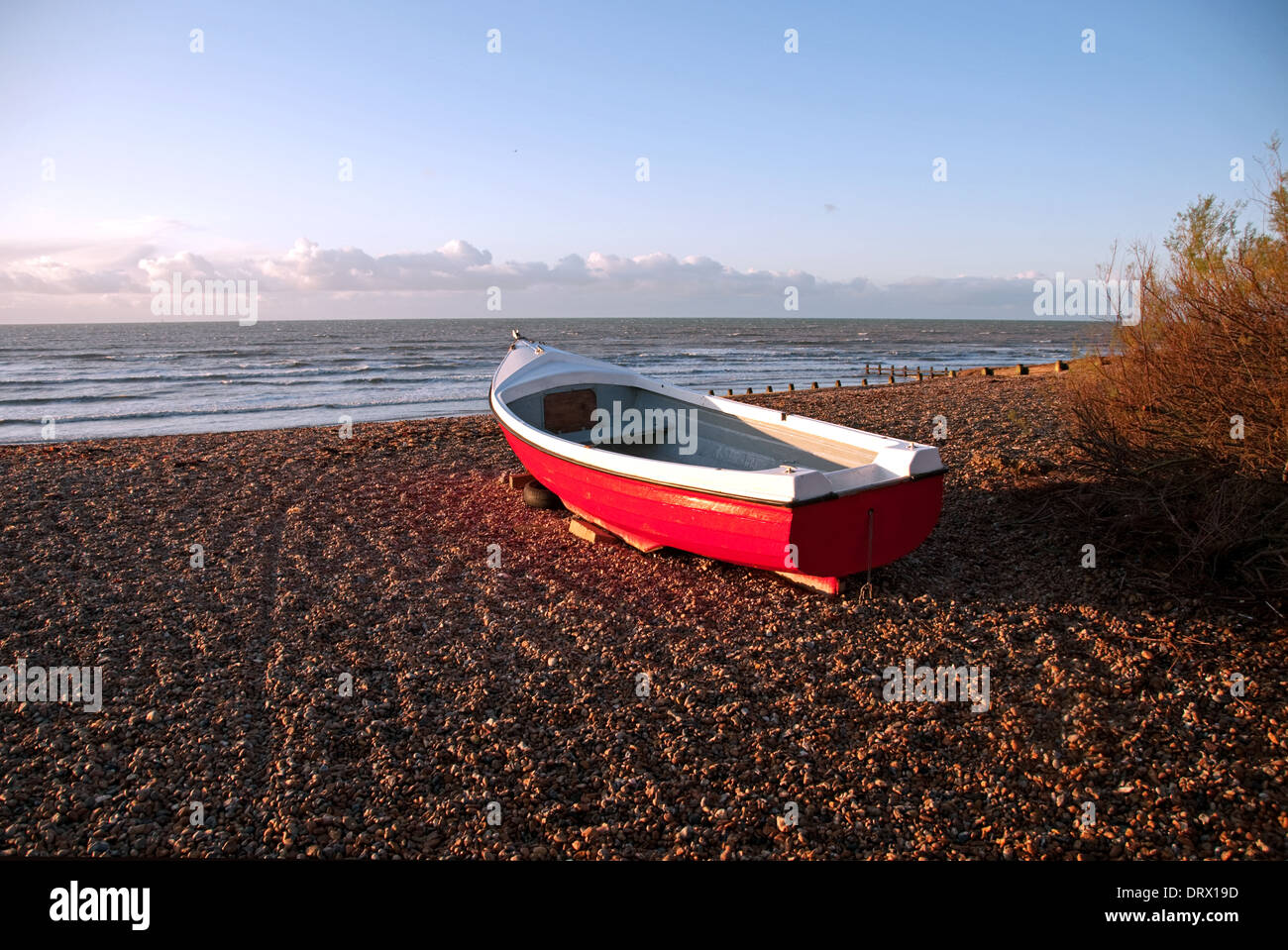Rosso barca sulla spiaggia di ciottoli, Angmering sul mare, West Sussex. Foto Stock