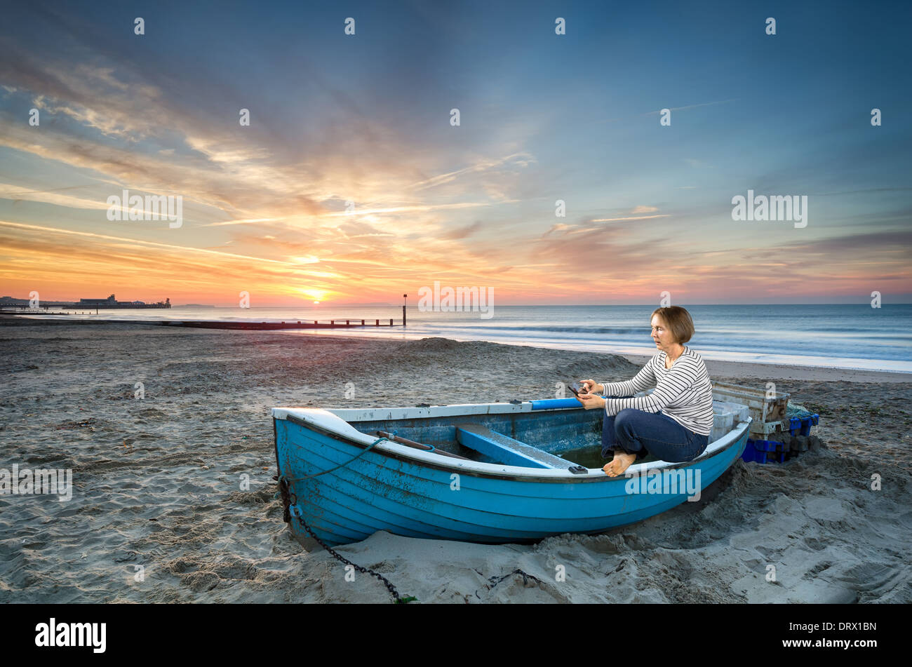 Donna matura in 50's utilizzando dispositivo tablet pc al sorgere del sole su una spiaggia idilliaca Foto Stock