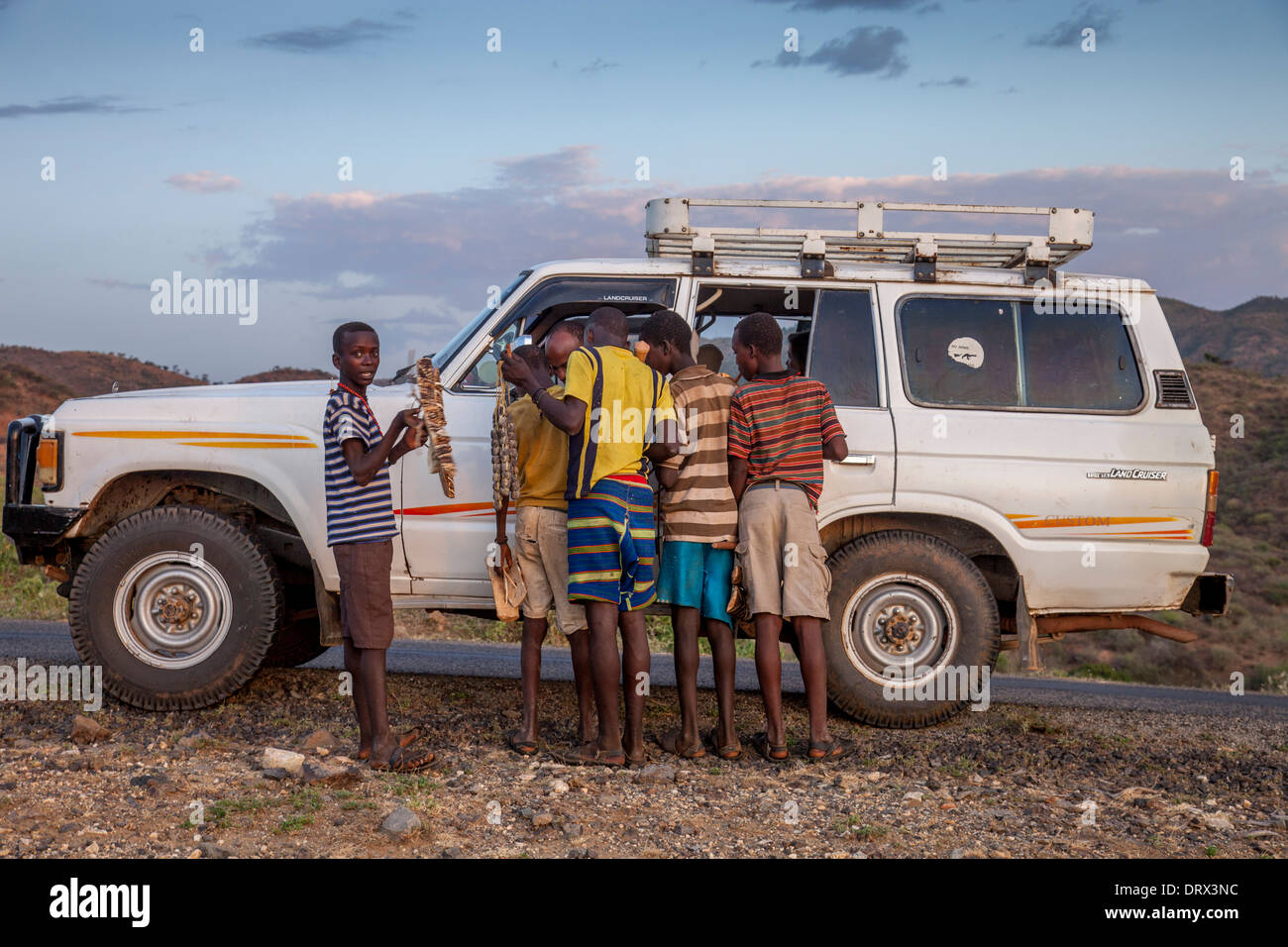 Ragazzi locali approccio un veicolo turistico per la vendita di prodotti artigianali, nella valle dell'Omo, l'Etiopia meridionale, Africa Foto Stock