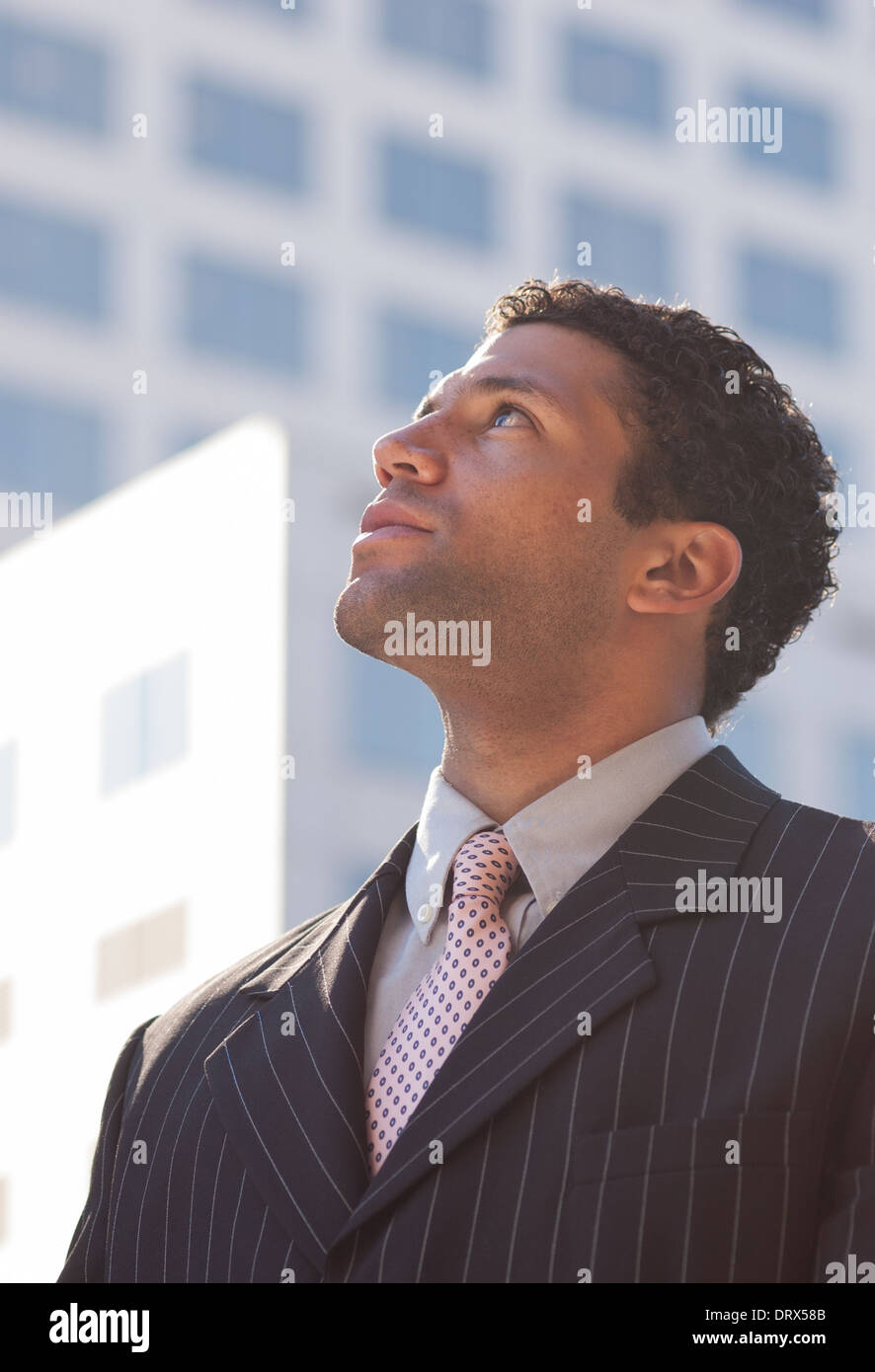 Nero uomo d'affari cerca su ritratto preso contro un edificio aziendale dello sfondo. Egli sembra ambizioso e orientato a un obiettivo. Foto Stock