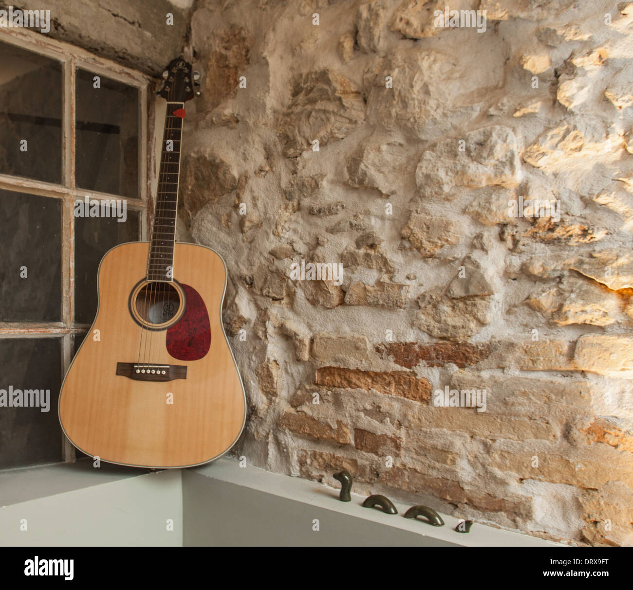 Chitarra acustica appoggiata contro la pietra rustica parete. Foto Stock