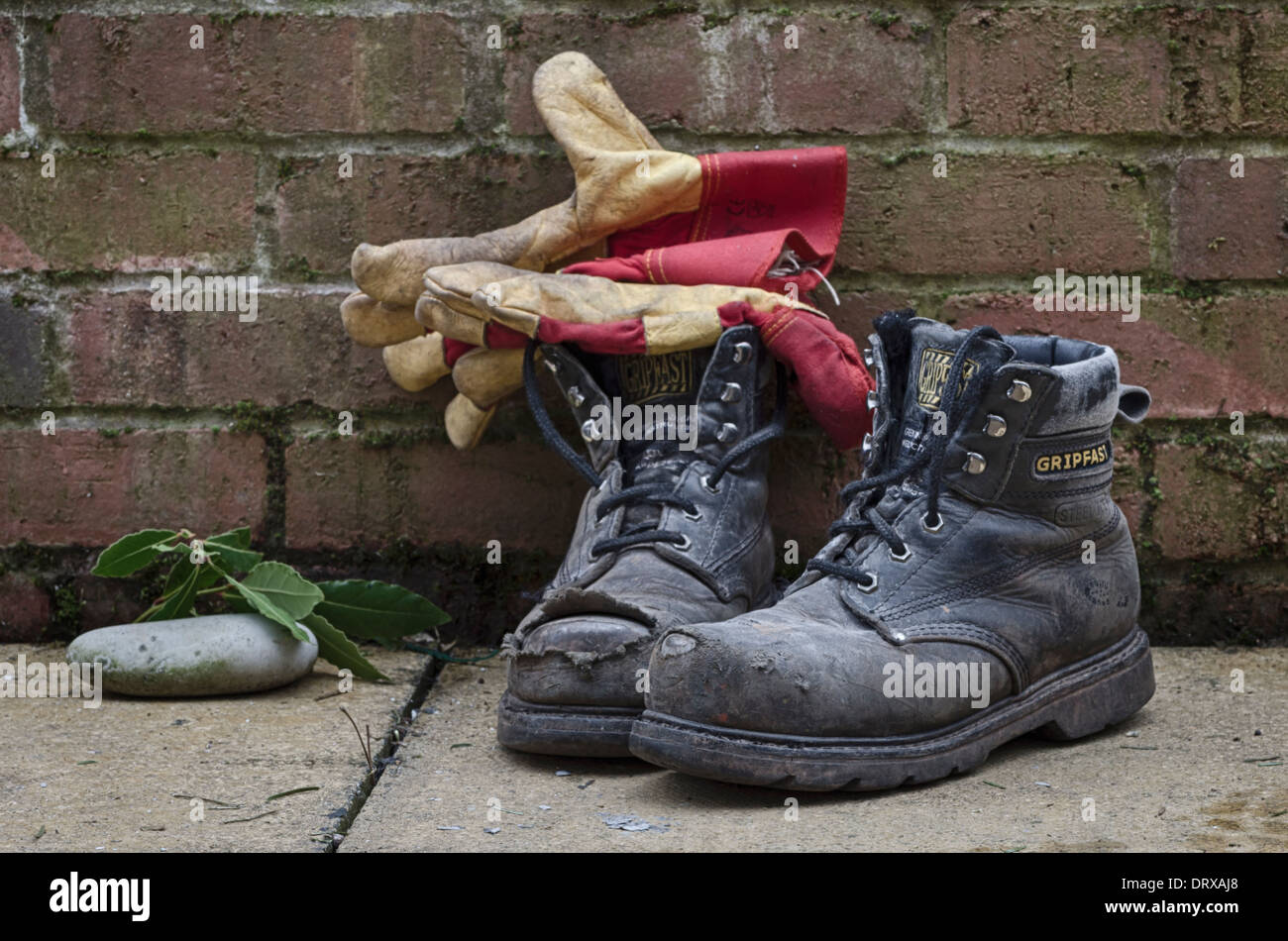 Una coppia di vecchi stivali da lavoro in giardino da un muro con un paio di guanti da giardinaggio Foto Stock