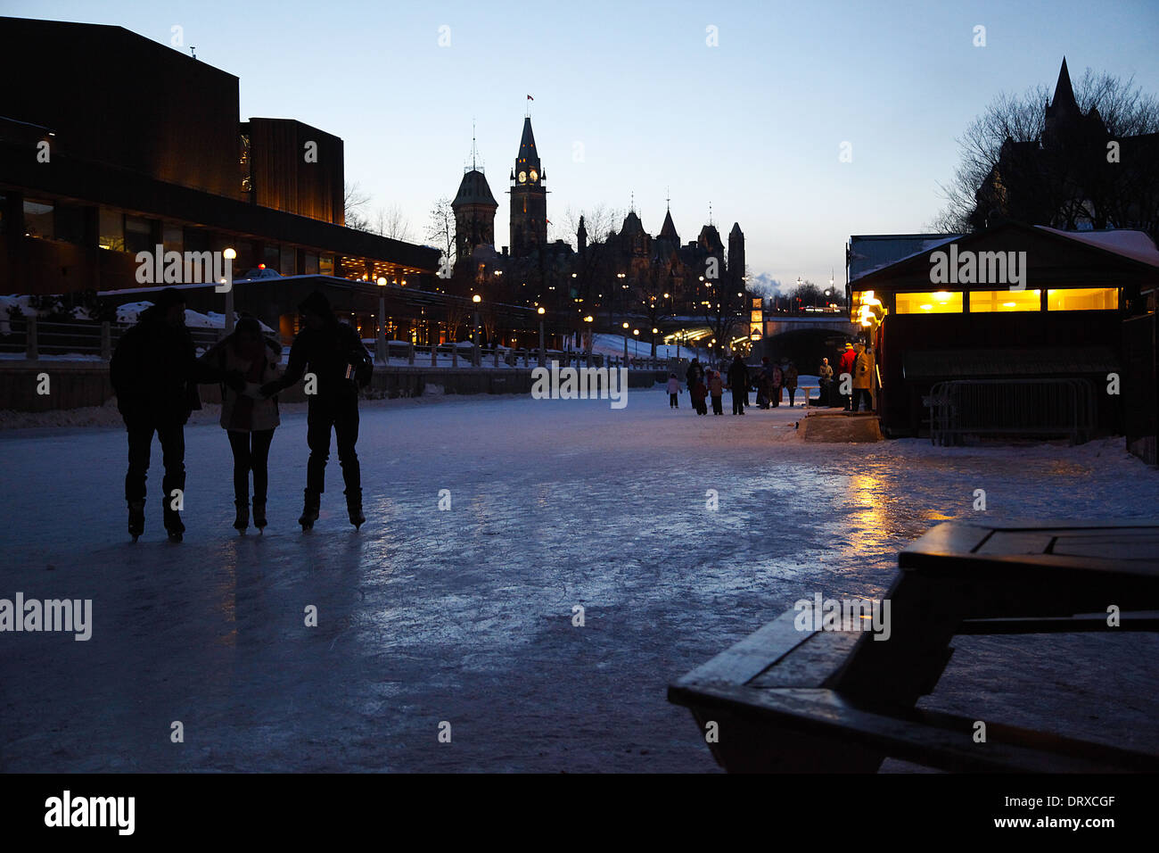 Tre sagome pattino lungo il canale Rideau in Ottawa, Ontario, Canada, la città e gli edifici del Parlamento europeo in background. Foto Stock