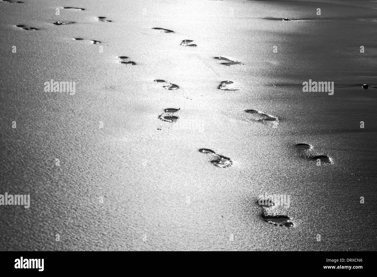 Una foto in bianco e nero di impronte su una spiaggia a croce diagonalmente una spiaggia. Foto Stock