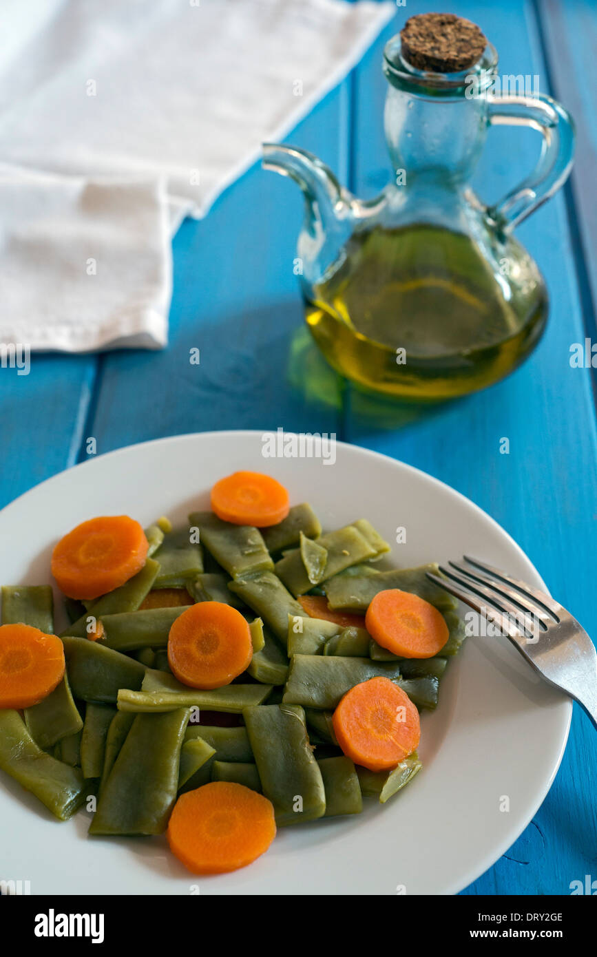 Insalata di fagioli verdi e carote nel piatto bianco su un tavolo blu accanto a un olio Foto Stock
