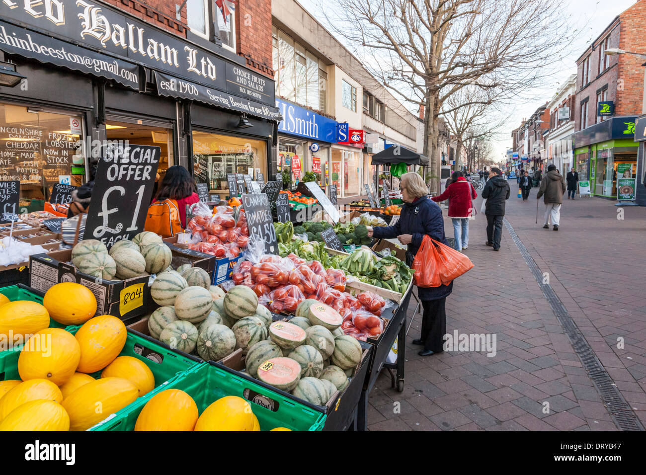 Persona per negozi di frutta e verdura presso un fruttivendolo tra gli altri negozi locali su una strada pedonale, Beeston, Nottinghamshire, England, Regno Unito Foto Stock