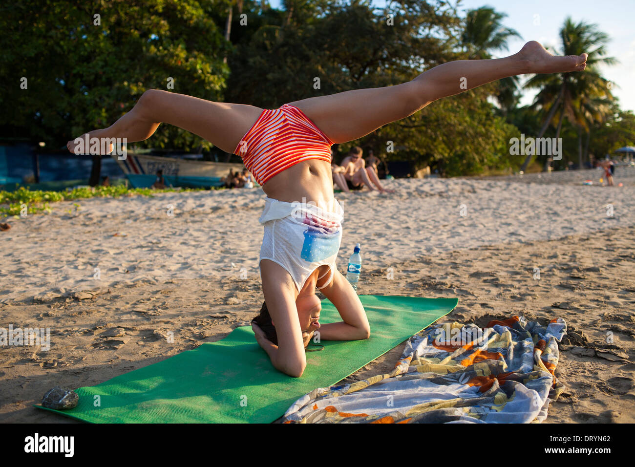 Una donna esegue una posa yoga o bilanciamento del movimento sul suo capo sulla spiaggia a Playa Tamarindo Guanacaste Costa Rica Foto Stock