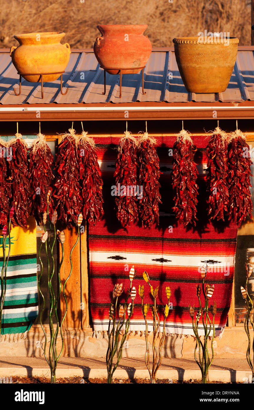 Peperoni secchi, tappeti e vasi di ceramica visualizzati contro una struttura di adobe e illuminato dal tardo pomeriggio sun. Foto Stock
