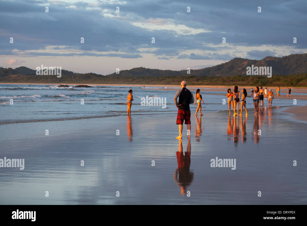Gruppi di persone di alzarsi e di camminare sulla Playa Tamarindo al tramonto, le loro immagini riflettono in sabbia a bassa marea in Guanacaste. Foto Stock