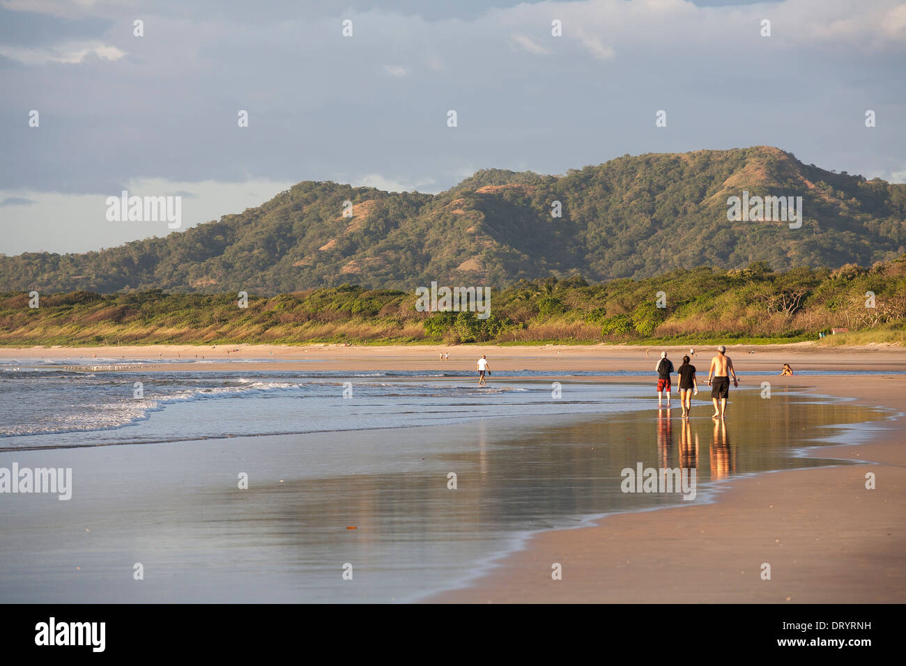 Gruppi di persone di alzarsi e di camminare sulla Playa Tamarindo al tramonto, le loro immagini riflettono in sabbia a bassa marea in Guanacaste. Foto Stock