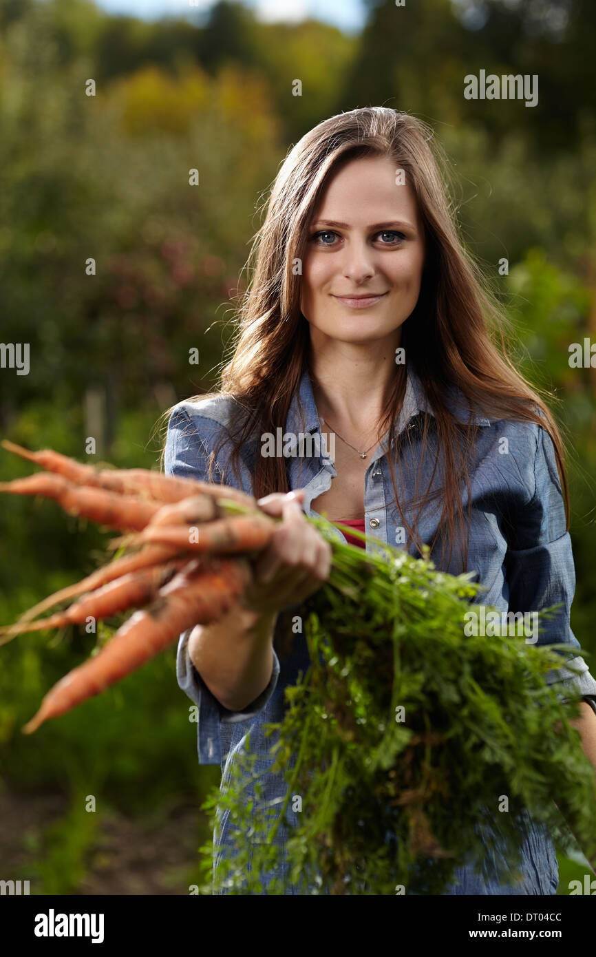 Giovane donna giardiniere tenendo un covone di carote nel suo giardino, il fuoco selettivo Foto Stock