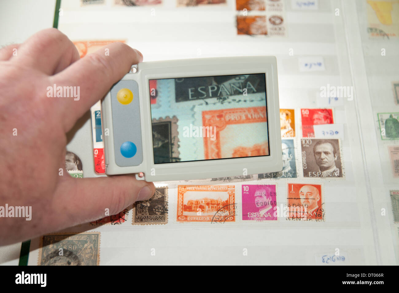 Una visione alterata stamp collector utilizza un dispositivo elettronico di lente di ingrandimento per ispezionare un timbro nella sua raccolta di francobolli Foto Stock