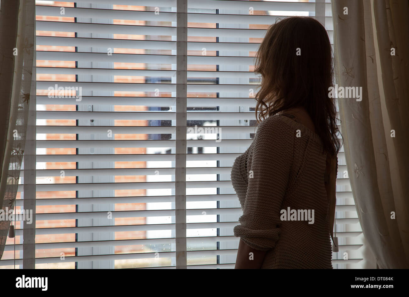 Silhouette di donna che indossa una vestaglia guardando fuori della finestra. Sulla spalla vista posteriore/laterale. Foto Stock