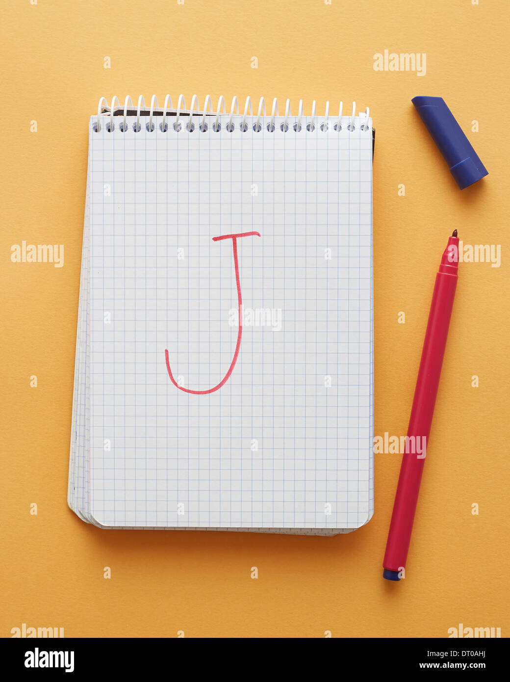 J Lettera scritta a mano nella pagina del notebook su sfondo giallo alfabeto Foto Stock