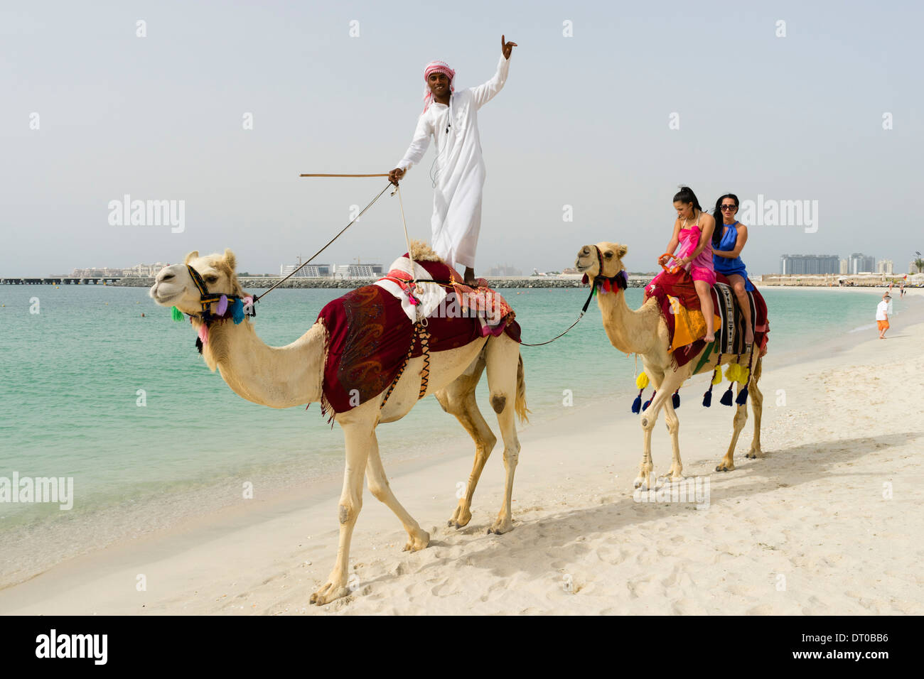 I turisti facendo un giro in cammello sulla spiaggia di Marina District di New Dubai negli Emirati Arabi Uniti Foto Stock