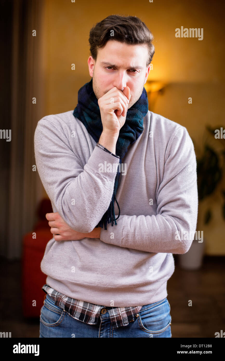 Giovane uomo a casa malato, tosse, con la mano davanti alla bocca Foto Stock