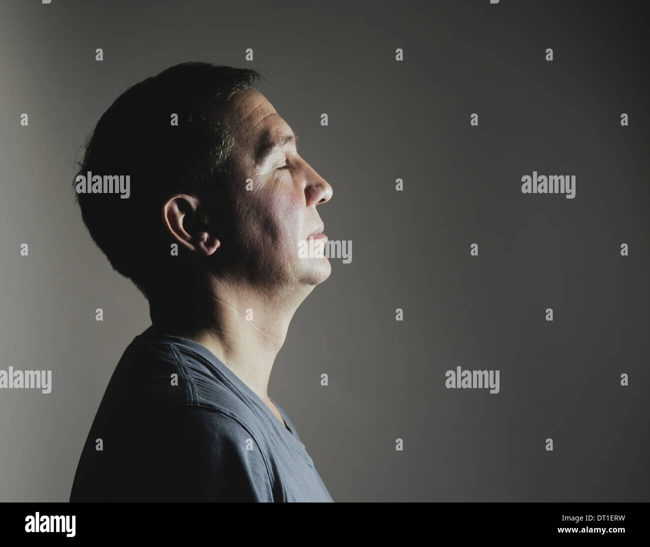 Un uomo seduto ancora in riposo con gli occhi chiusi visto di profilo di una sorgente di luce che rifulge sul suo volto Foto Stock