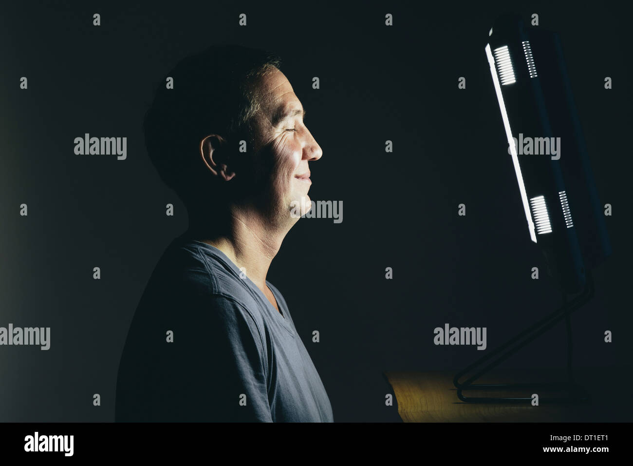 Sorridente uomo di mezza età seduto di fronte a una terapia a base di luce casella trattamento di affetti da disturbo affettivo stagionale Foto Stock