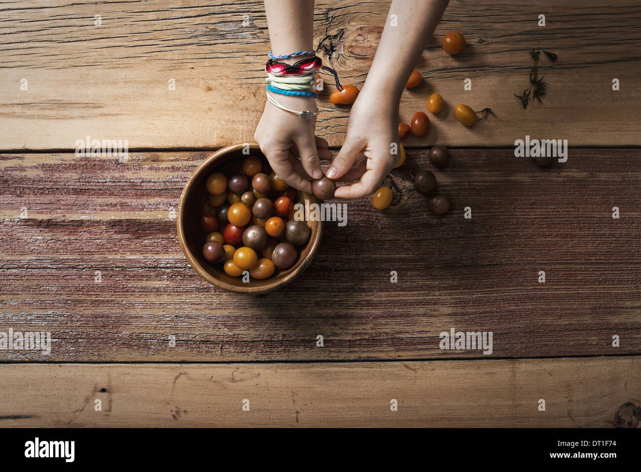 Un recipiente rotondo con pomodorini di vari colori e una persona smistamento e prelievo su di loro un tavolo in legno Foto Stock