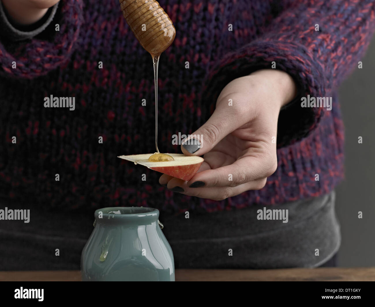 Una donna drizzling miele da un tondo in legno stick pioggerellina su di una fetta di Apple Foto Stock