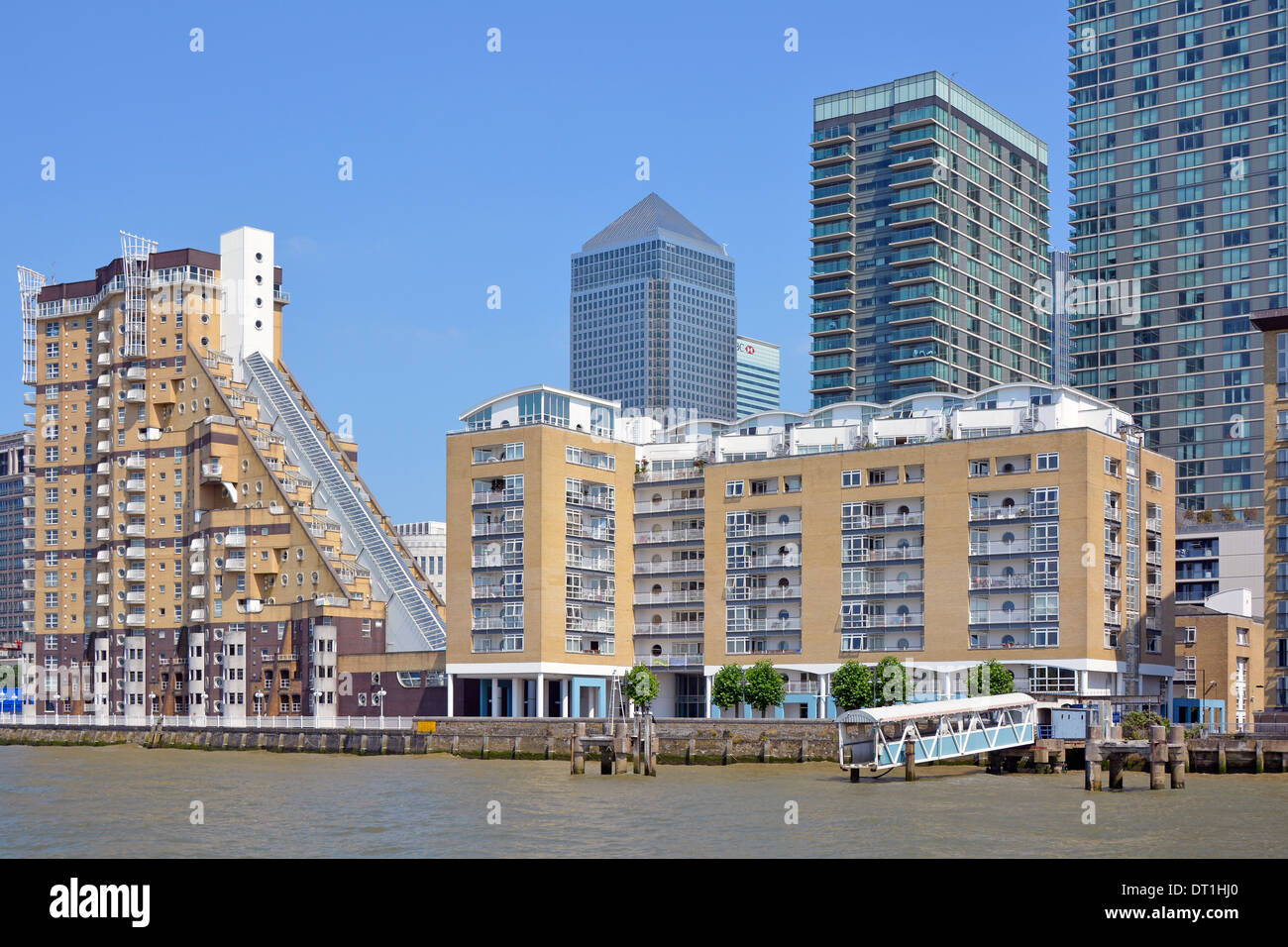 Moderno complesso di appartamenti sul mare accanto al Tamigi con Canary Wharf pietra miliare grattacieli blocchi di uffici oltre il cielo blu giorno a East London Regno Unito Foto Stock