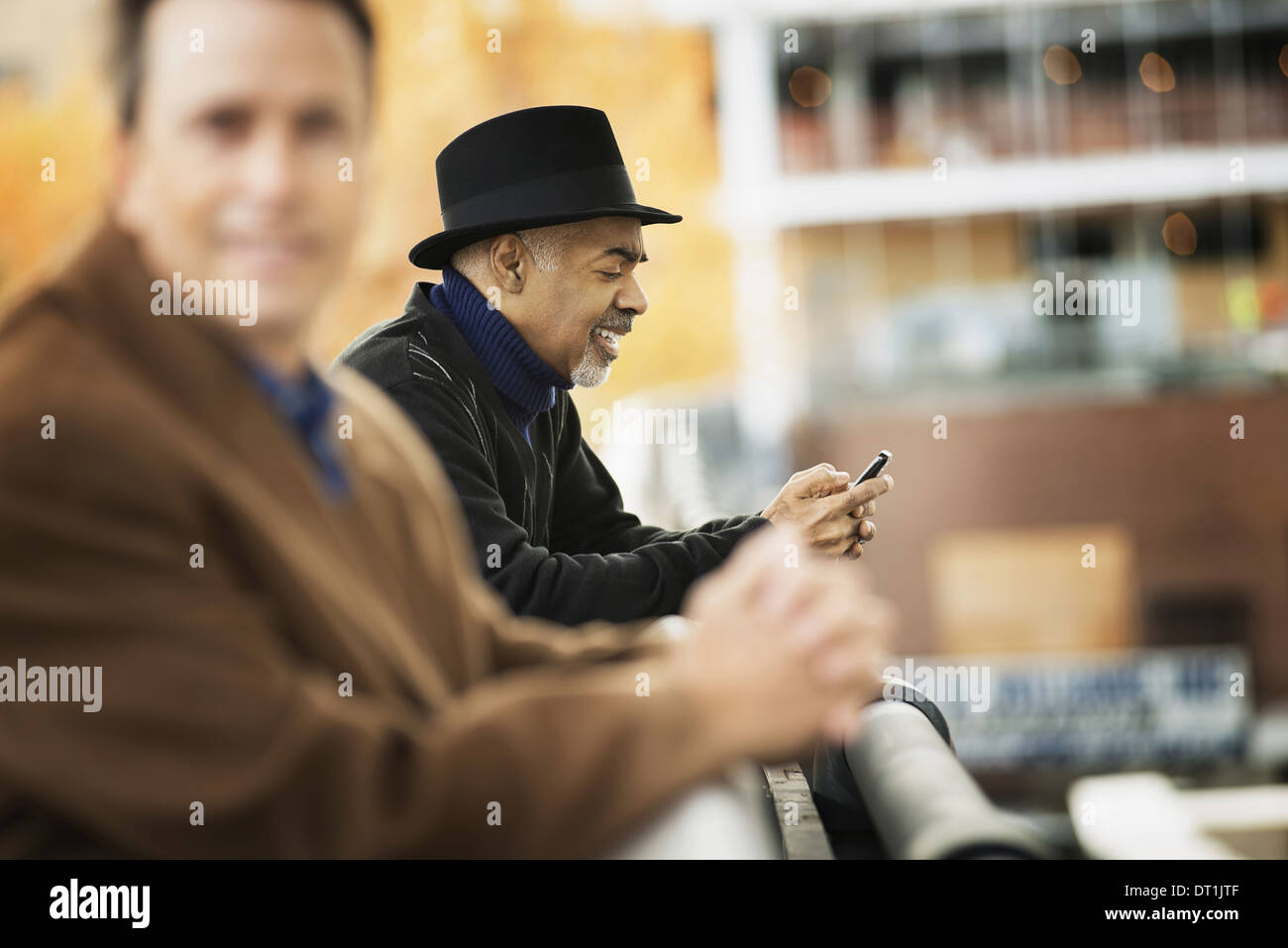 Professionisti in movimento di mantenere in contatto utilizzando i telefoni cellulari due uomini in cappotti appoggiato su di una ringhiera Foto Stock