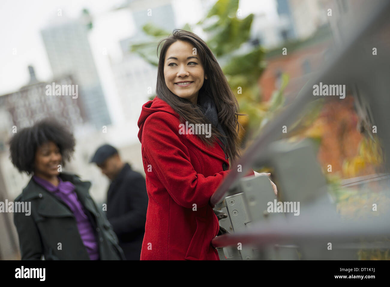 Una donna in un rosso cappotto appoggiato su di una ringhiera due persone sullo sfondo del paesaggio della città di edifici Foto Stock