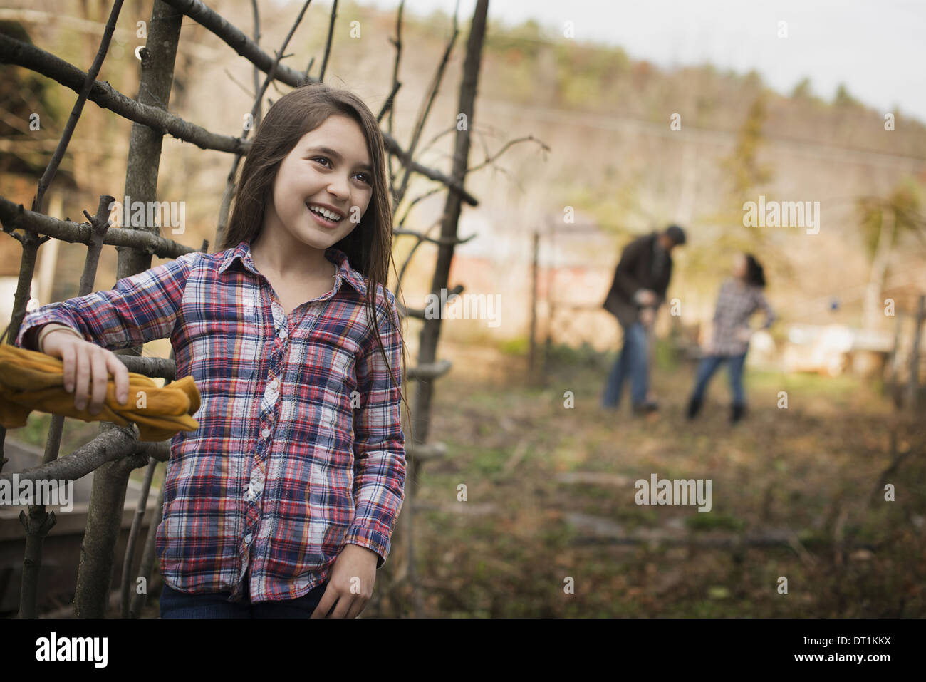 Una giovane ragazza appoggiato su di una recinzione e due persone sullo sfondo di una azienda agricola biologica Foto Stock