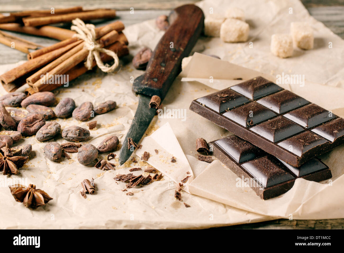Il cioccolato fondente con il vecchio coltello, le fave di cacao, cannella e anice su carta sgualcita su sfondo di legno. Vedere serie Foto Stock