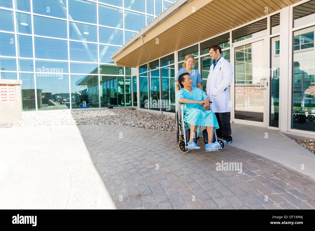 Infermiera e medico guardando il paziente su una sedia a rotelle al cortile Foto Stock