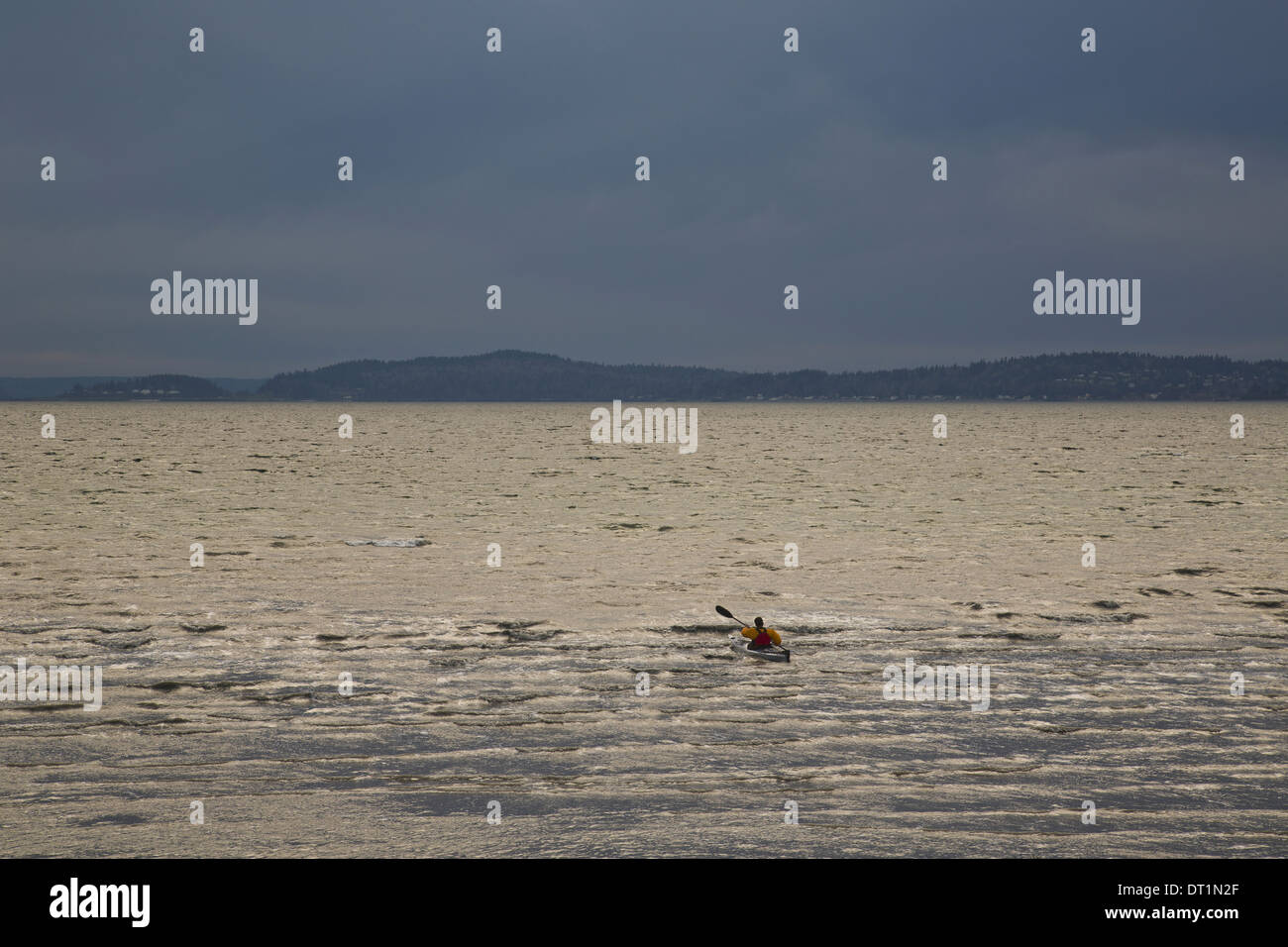 Un kayaker pagaie suo kayak di mare nel Puget Sound su un colore scuro e nuvoloso sera Foto Stock