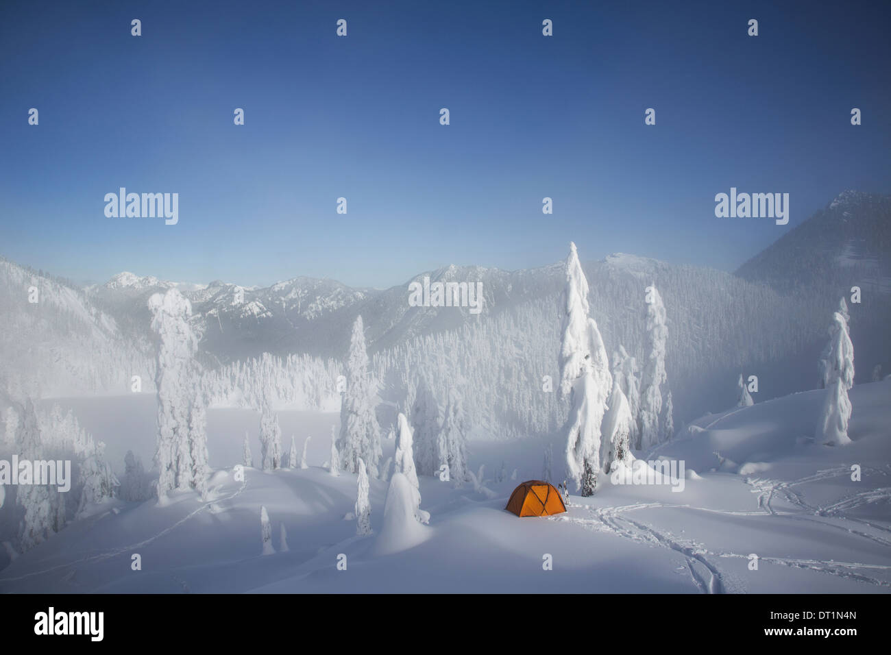 Una luce arancione brillante tenda tra coperta di neve alberi su un crinale nevoso si affaccia su una montagna a distanza Foto Stock