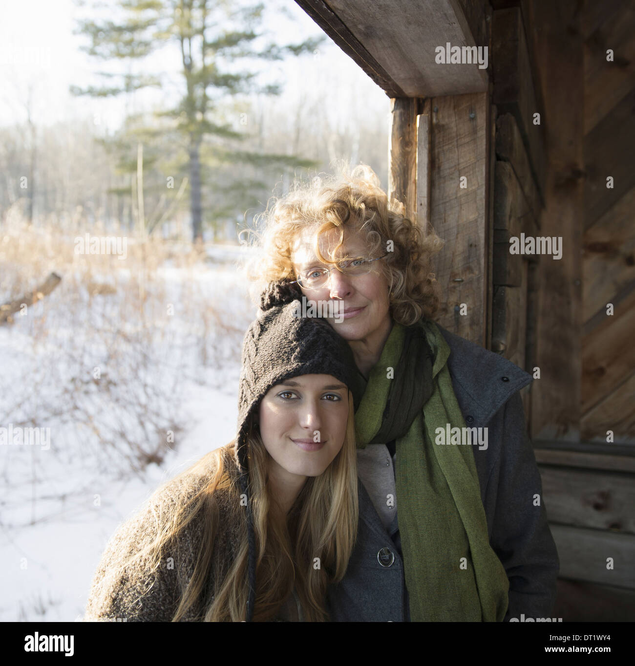 Due persone una madre e figlia fianco a fianco nel portico di una capanna di legno su una fattoria di una giornata invernale e Foto Stock