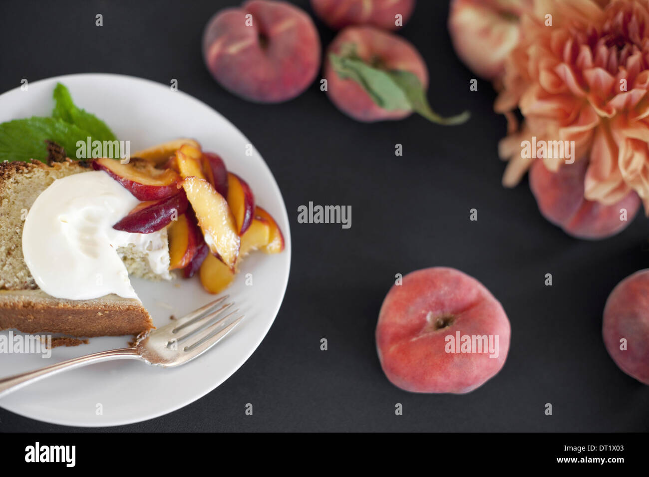 Una tabella visualizzata dalla testa di frutta pesche e fiori una piastra con la torta di frutta fresca e creme fraiche una forcella Dessert Foto Stock
