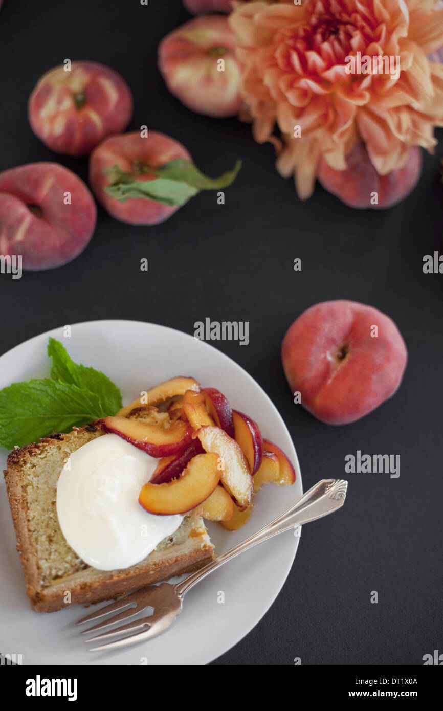 Una tabella visualizzata dalla testa di frutta pesche e fiori una piastra con la torta di frutta fresca e creme fraiche una forcella Dessert Foto Stock
