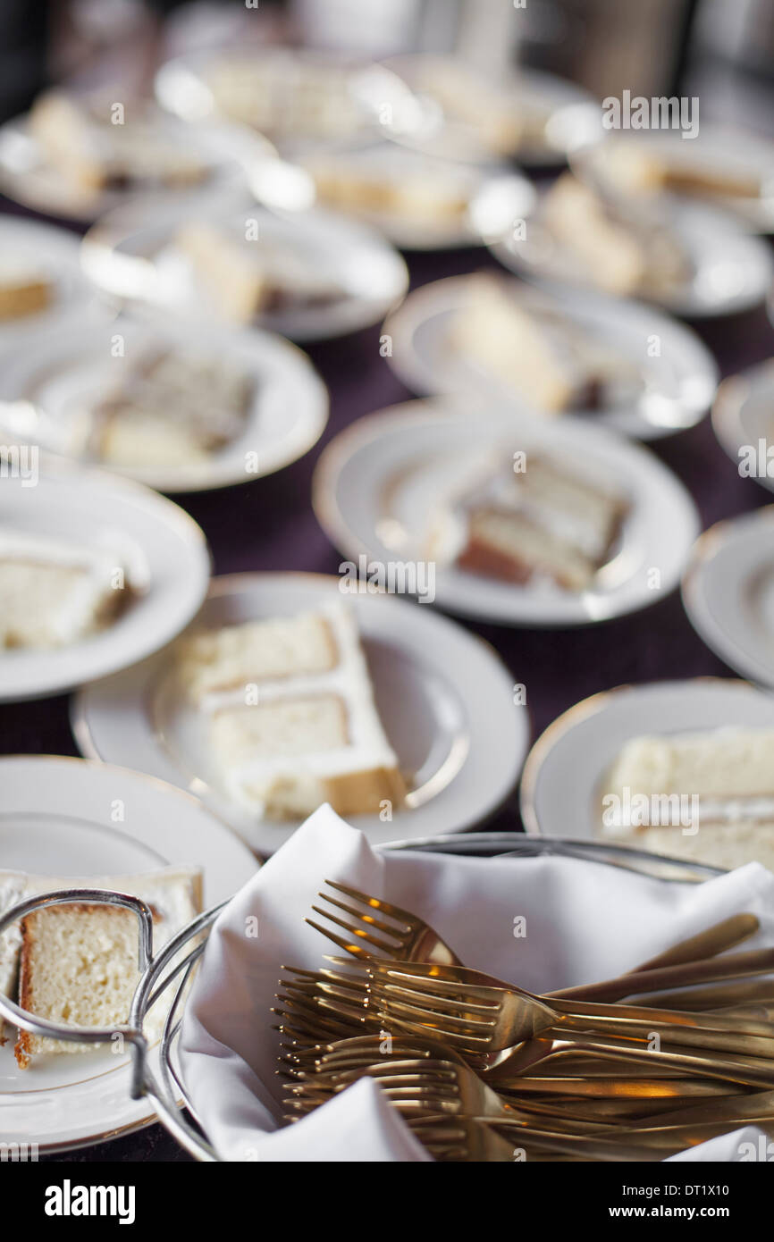 Una tabella laden con placche in porcellana bianca e un cesto pieno di dessert forche una fetta di torta di nozze Foto Stock