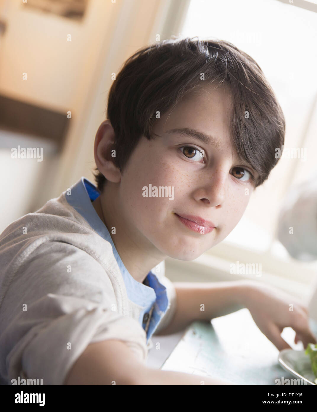 Un bambino di un giovane ragazzo con capelli castani e gli occhi castani seduto a tavola con la famiglia Foto Stock