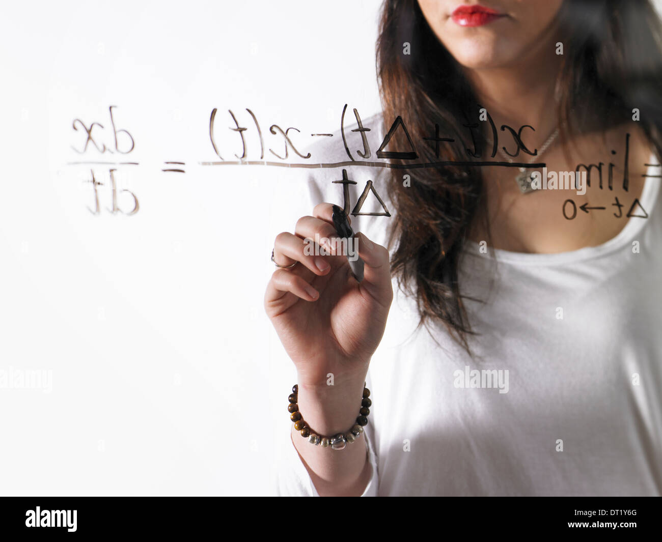 Una giovane donna a scrivere una equazione matematica con pennarello nero su un chiaro vedere-attraverso la superficie Foto Stock