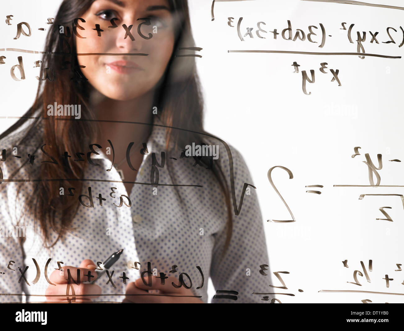 Una giovane donna che guarda ad una equazione matematica scritta con pennarello nero su un chiaro vedere-attraverso la parete Foto Stock